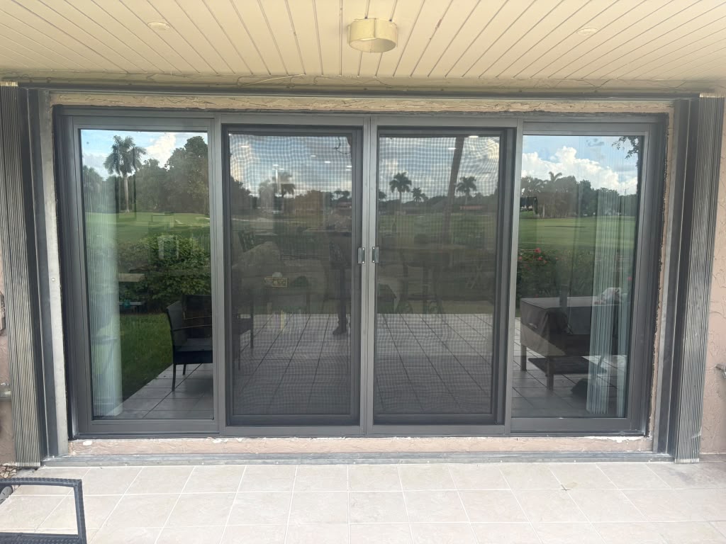 New four-panel dark-bronze impact sliding glass door after installation overlooking a golf course