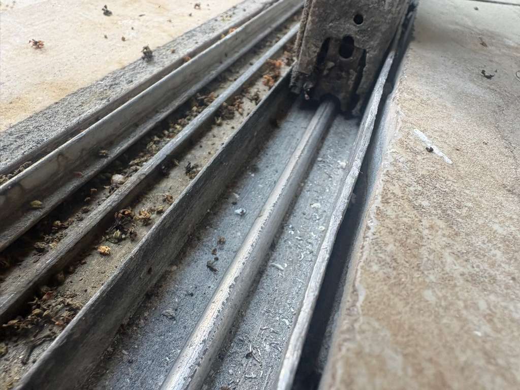Dirty, worn sliding glass door track before being cleaned and rebuilt